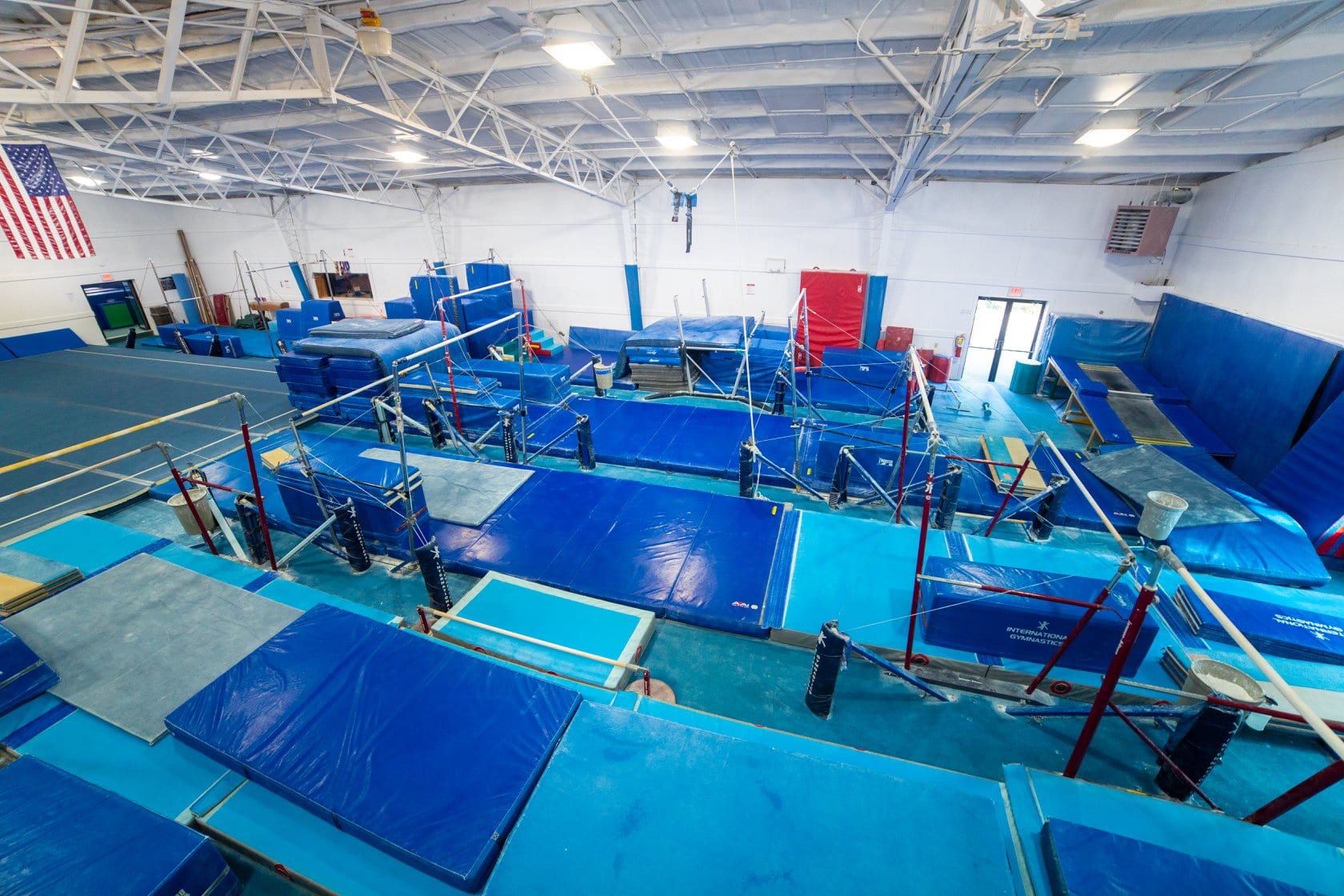 Indoor gymnastics facility with various blue mats and equipment under bright lighting.