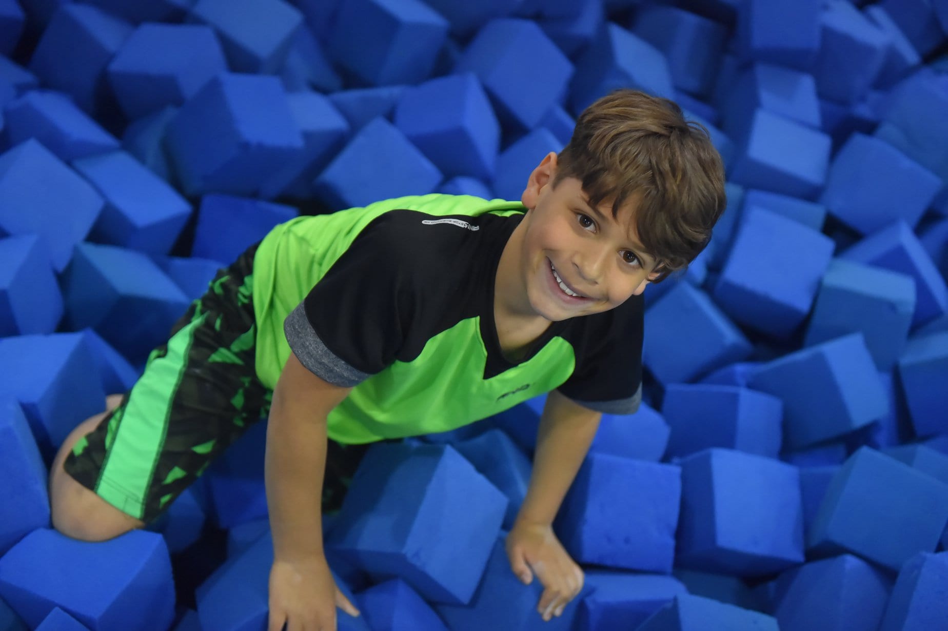 Boy playing in a foam pit with blue foam blocks.