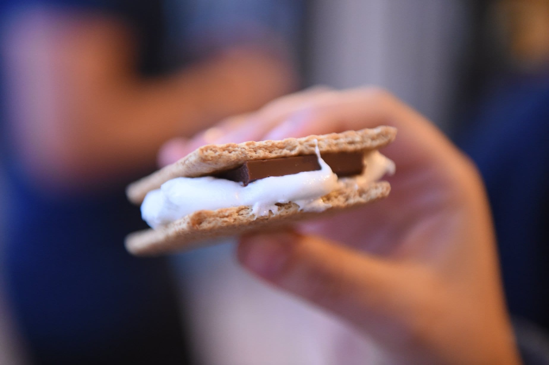 A hand holding a s'more with melted chocolate and marshmallow.