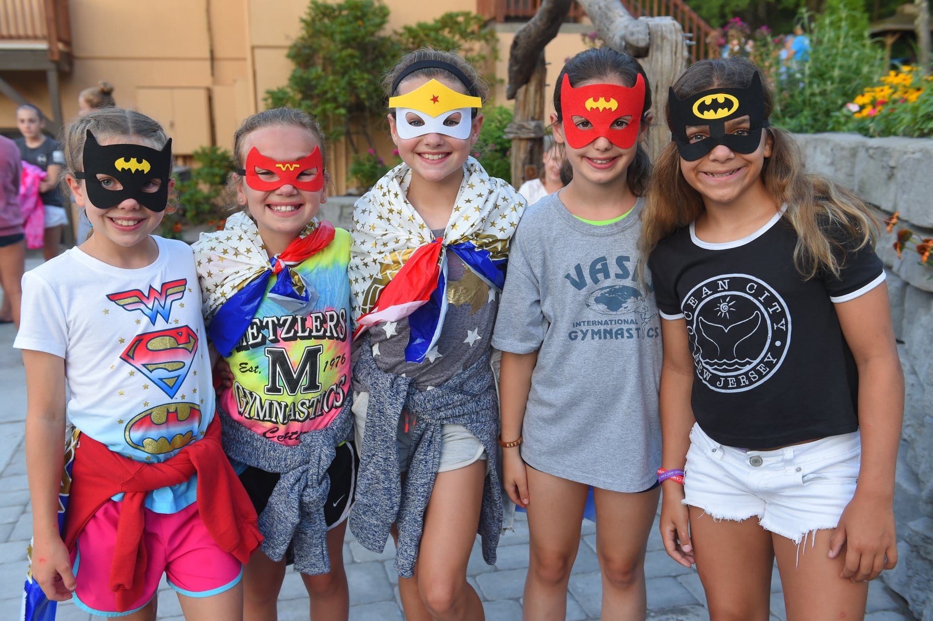 Four kids in superhero masks smiling outdoors.