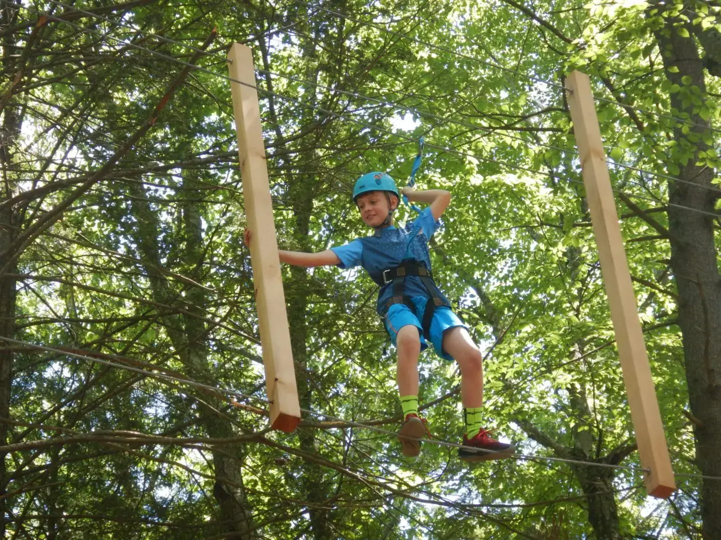 Child balancing on ropes course high above ground in forest.