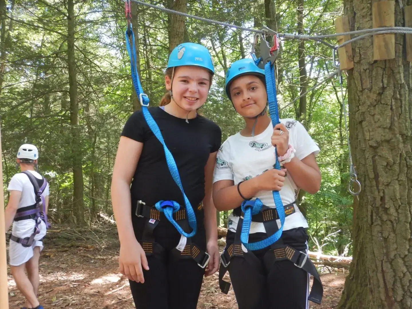 Two people in helmets posing with zipline harnesses in a forest.